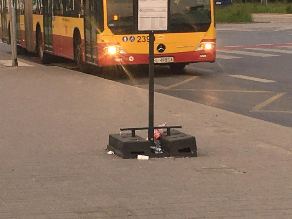 Podróżni MPK Łódź oczekują na autobus na przystanku bez wiaty, ławki i śmietnika.